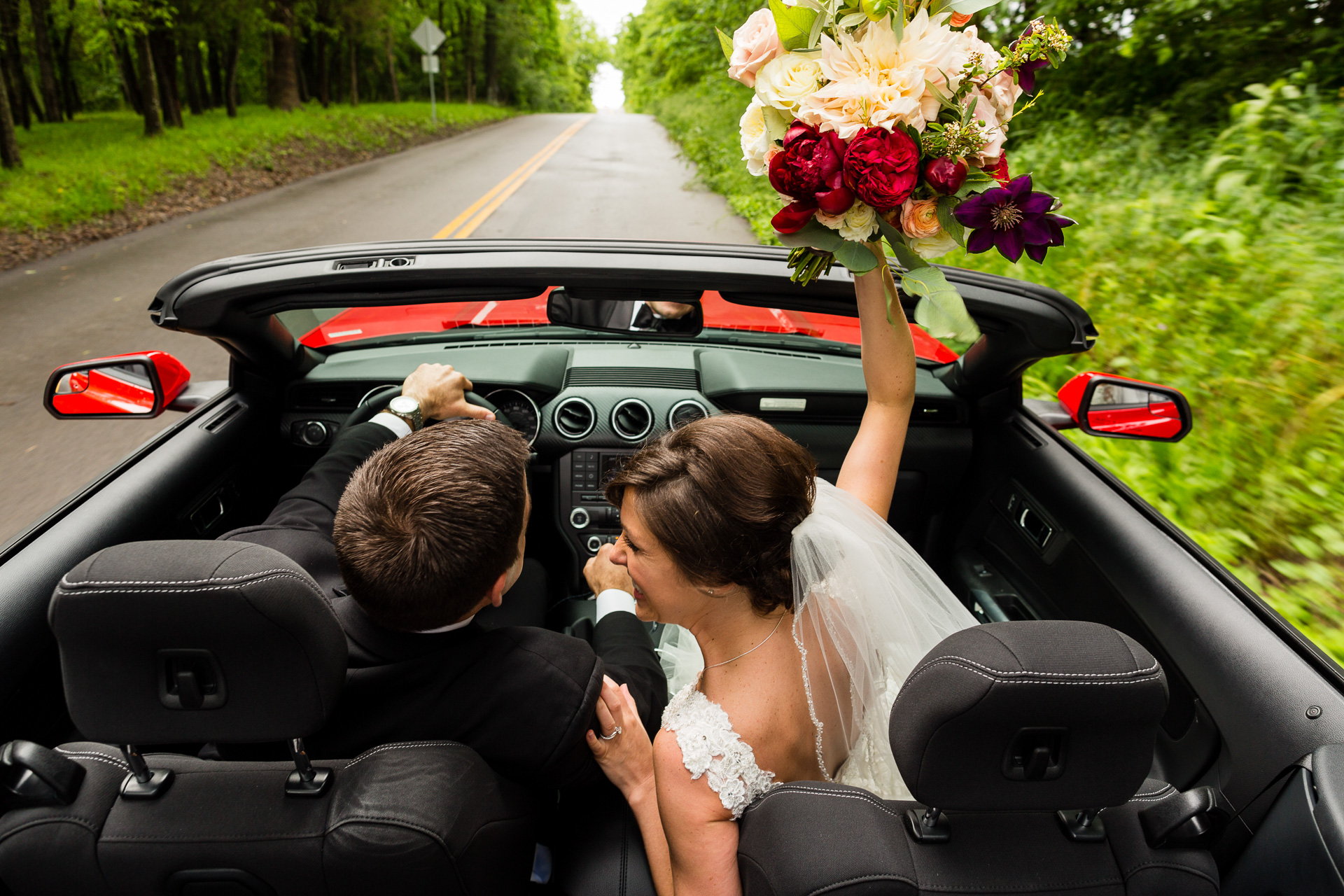 bride groom looking at each other driving convertible bouquet in the air