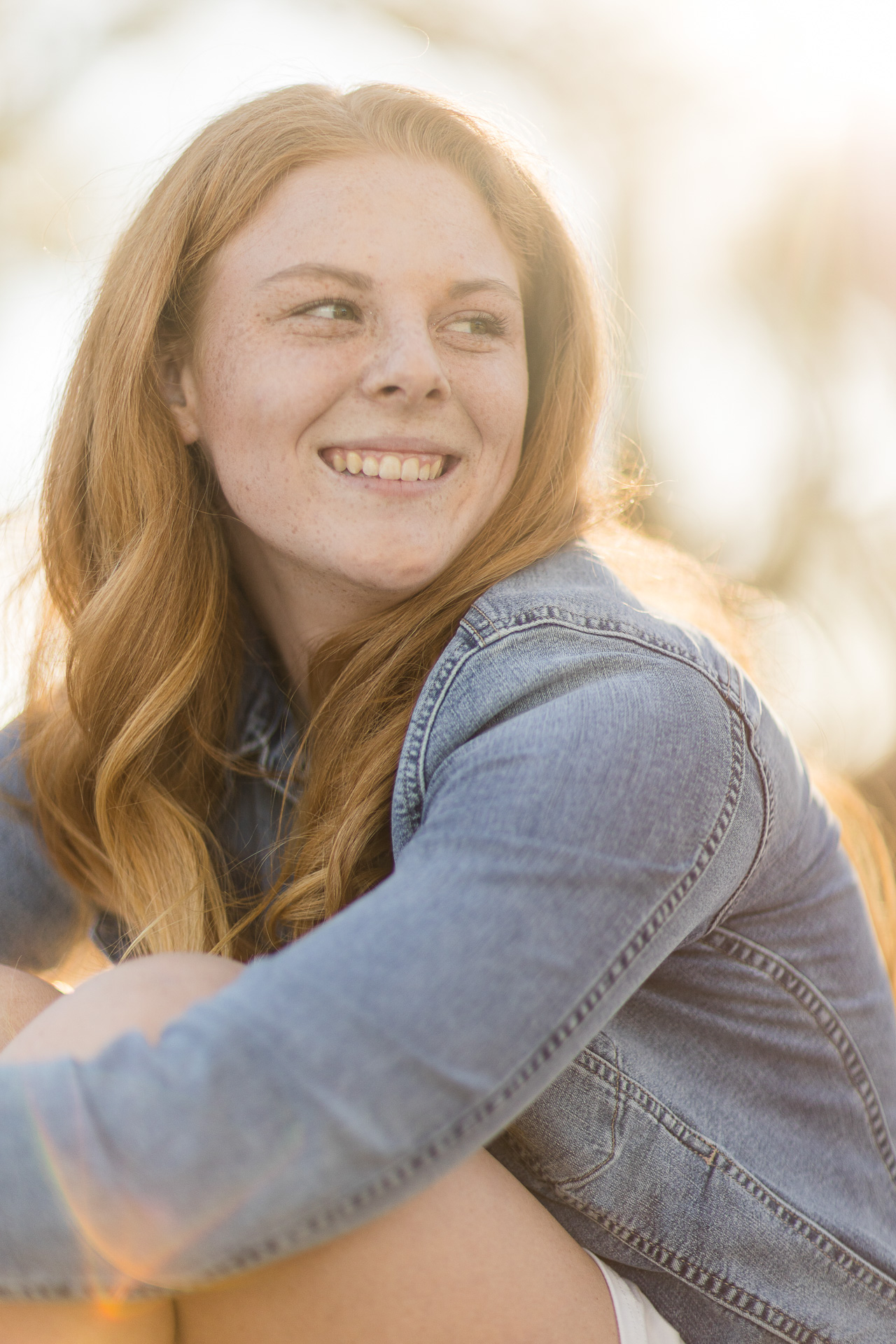 female redhead high school senior sitting while looking away from camera during sunset