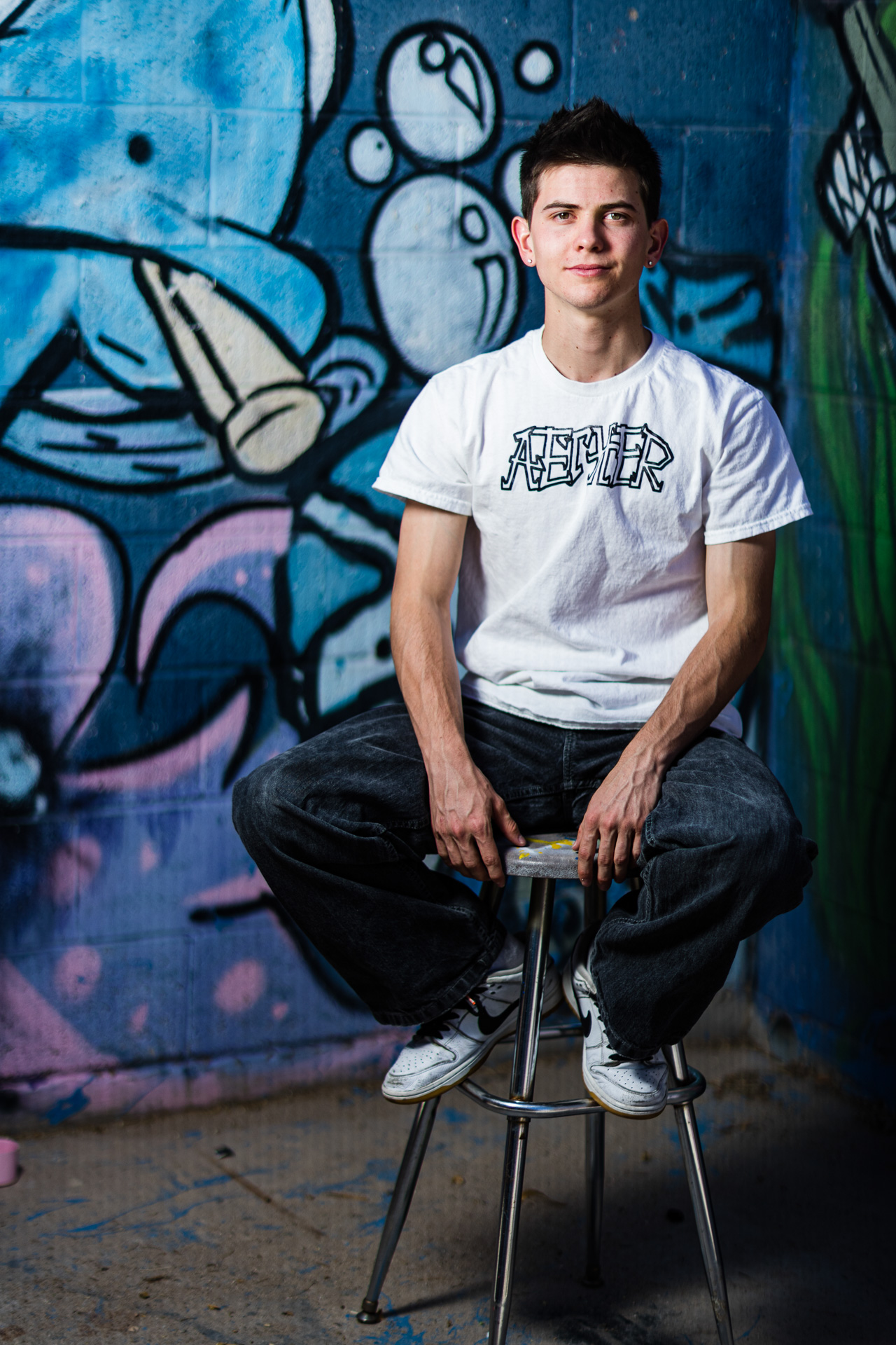 Male High School Senior sitting on bar stool with graffiti background