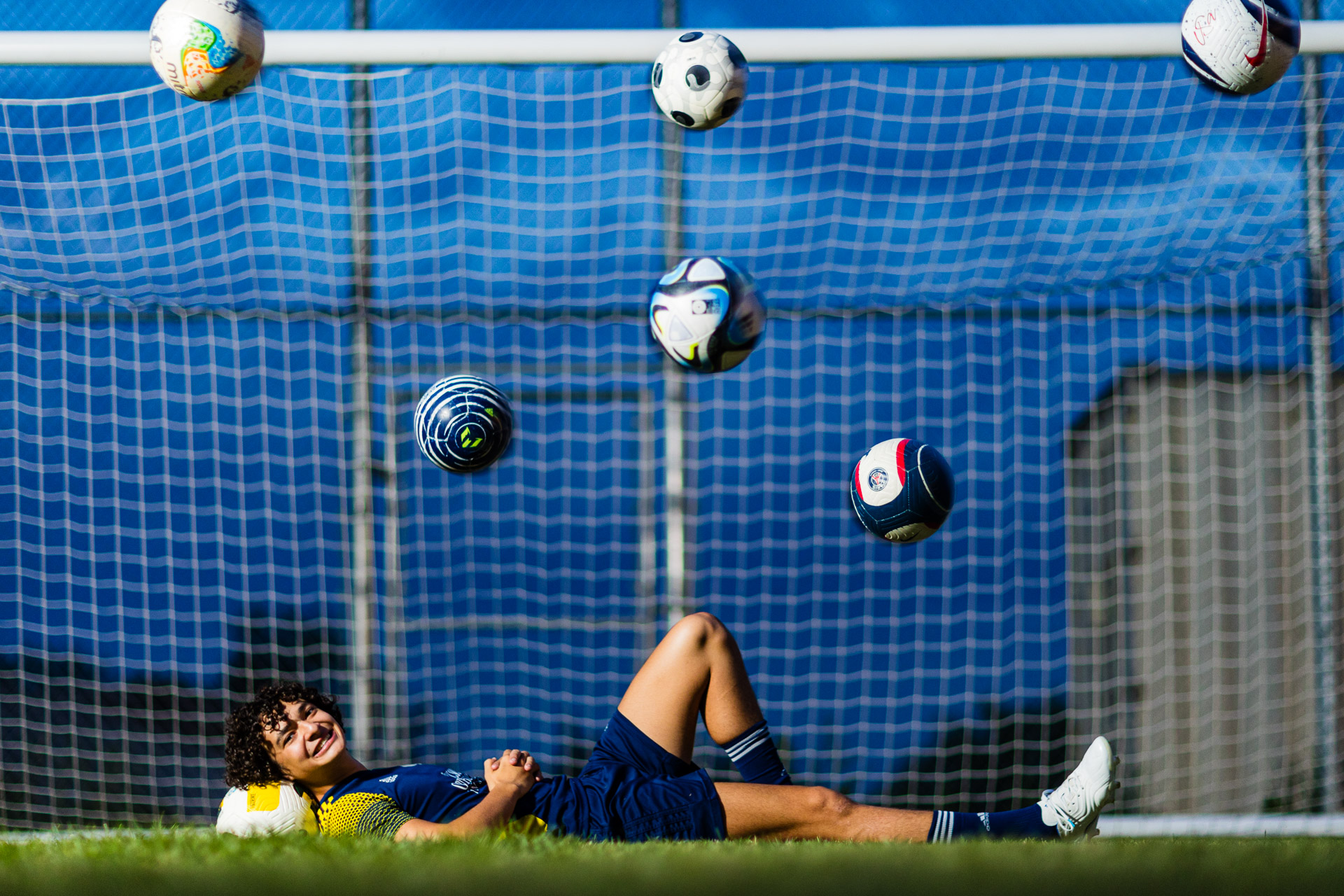 male high school senior soccer player laying down with multiple balls in the air